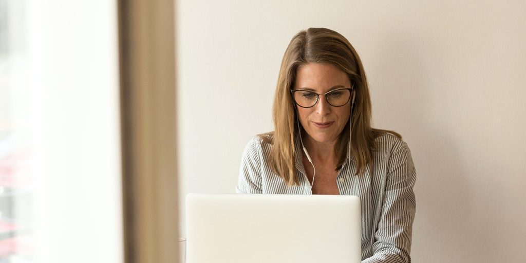 Frau mit Brille arbeitet konzentriert an Laptop, heller Bürohintergrund, EQWAL flexibler Overflow-Support.