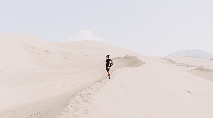 Person wandert auf Sanddüne unter blauem Himmel, symbolisiert Herausforderungen in Rechtsabteilungen.
